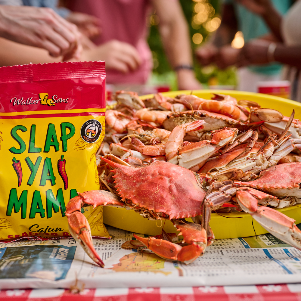 Louisiana blue crabs on a seafood tray placed on a table, with a bag of seafood boil nearby. People’s hands are peeling seafood in the background.