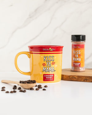 
                  
                    Load image into Gallery viewer, Kiss Ya Mama mug placed alongside a Kiss Ya Mama canister and spilled coffee beans on a white kitchen countertop, creating a cozy breakfast scene.
                  
                