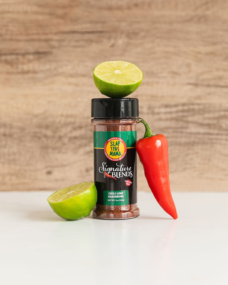 
                  
                    Load image into Gallery viewer, Lifestyle image of a Slap Ya Mama Chili Lime Signature Blend canister with a half lime cut open on top of the can, and another half lime and a chili pepper leaning against the side of the canister.
                  
                