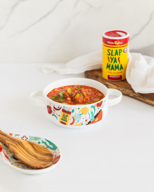 
                  
                    Load image into Gallery viewer, Lifestyle image of a Slap Ya Mama ceramic gumbo bowl filled with chili, placed on a white table with a wooden spoon and cutting board in the background. A Slap Ya Mama seasoning can is also visible in the scene.
                  
                