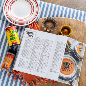 
                  
                    Load image into Gallery viewer, Open cookbook with recipe index on a wooden cutting board with spices and plates.
                  
                