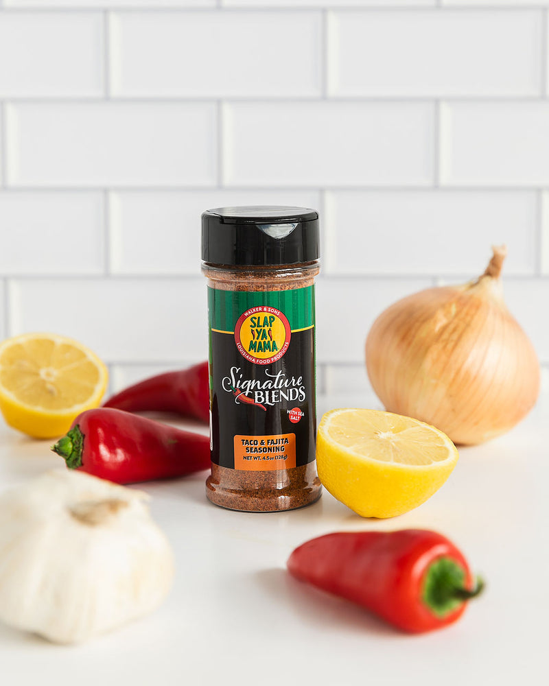 
                  
                    Load image into Gallery viewer, Slap Ya Mama Taco and Fajita Signature Blends seasoning canister styled in a vibrant scene with fresh ingredients, including a lemon, onion, garlic, and chili peppers, arranged on a rustic surface.
                  
                