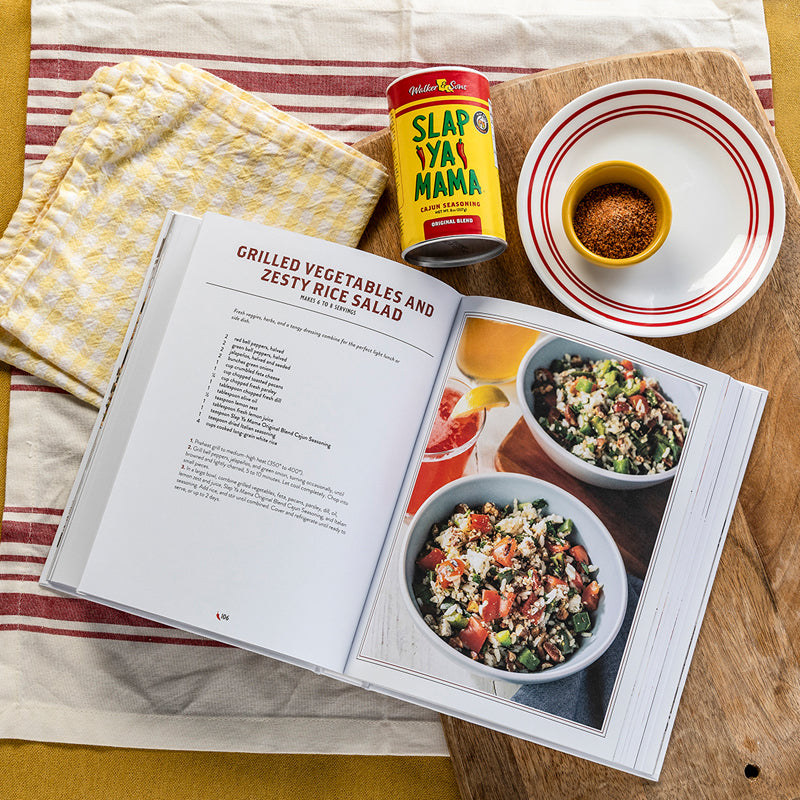
                  
                    Load image into Gallery viewer, Open cookbook with recipe for grilled vegetables and zesty rice salad, featuring a can of Slap Ya Mama seasoning.
                  
                