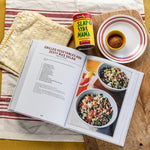 Open cookbook with recipe for grilled vegetables and zesty rice salad, featuring a can of Slap Ya Mama seasoning.
