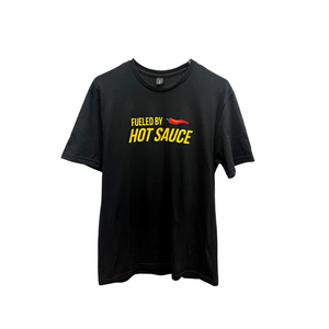 
                  
                    Load image into Gallery viewer, Black shirt with yellow text on the front reading &amp;#39;Fueled by Hot Sauce&amp;#39; accompanied by a pepper graphic.
                  
                