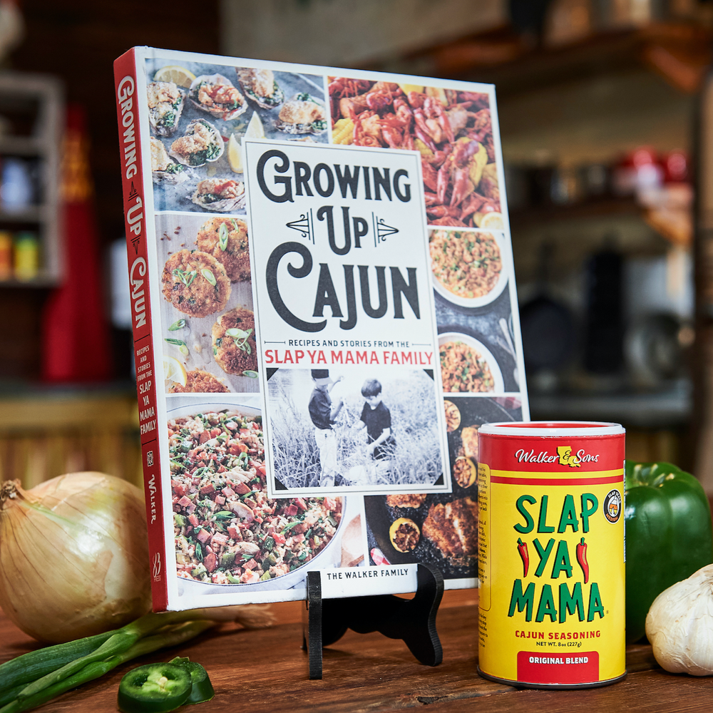 Cookbook 'Growing Up Cajun' on a kitchen counter with a Slap Ya Mama seasoning can placed next to it, surrounded by ingredients and a rustic kitchen atmosphere.