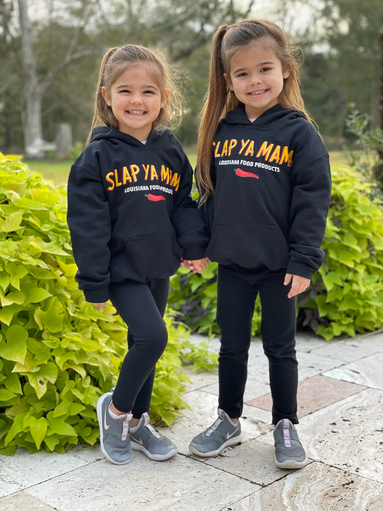 Two young girls wearing the black Slap Ya Mama hoodie with the yellow logo, standing outside, smiling and enjoying the moment.