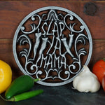 7-inch cast iron trivet with the Slap Ya Mama logo, placed on a wooden background with fresh vegetables surrounding it, creating a rustic and flavorful scene.