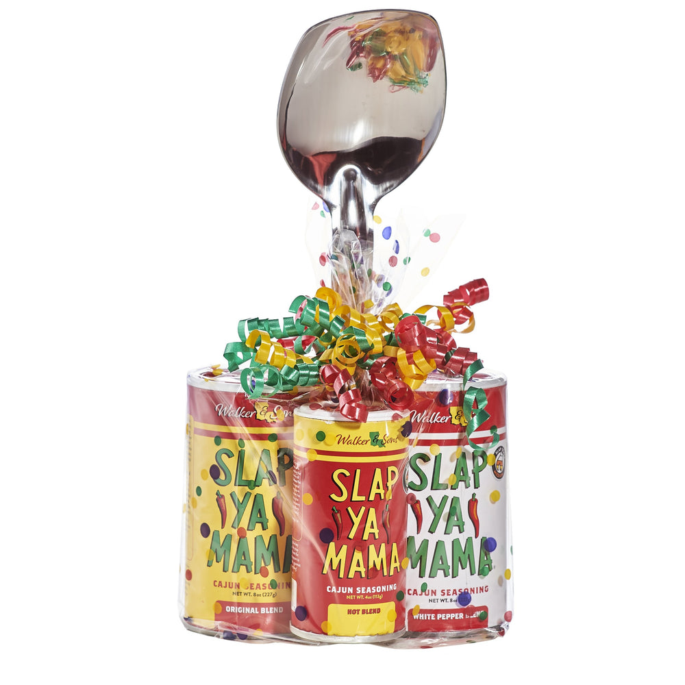 Gift set including an 8oz canister of Slap Ya Mama Original Blend Seasoning, 8oz canister of Slap Ya Mama White Pepper Blend Seasoning, 4oz canister of Slap Ya Mama Hot Blend Seasoning, and an 11-inch stainless steel roux spoon, wrapped in clear plastic with a ribbon, on a white background.
