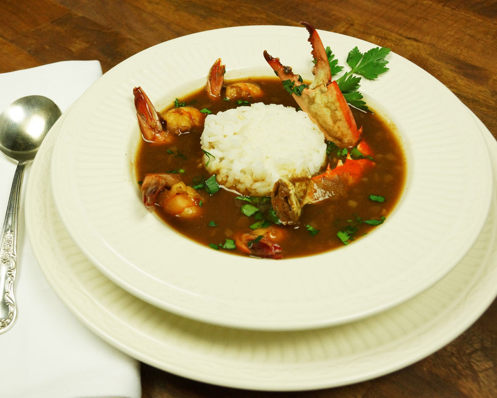 Bowl of shrimp and crab gumbo with a rich, dark roux, chunks of crab meat, plump shrimp, and white rice, garnished with chopped green onions